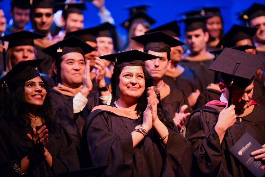 large group of MBA graduates at a commencement ceremony, clapping and smiling